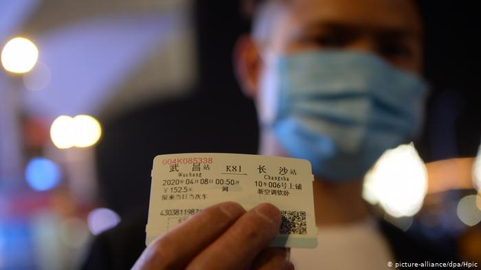 Человек в защитной маске держит в руках билет на поезд