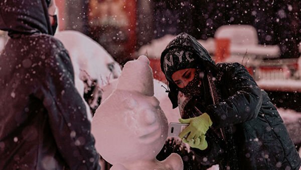 Женщина фотографируется со снеговиком на Таймс-сквер во время снегопада в Нью-Йорке