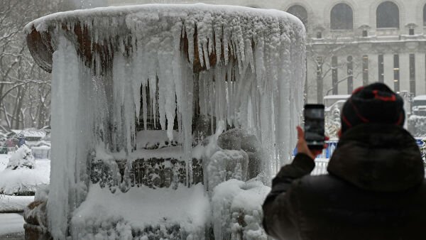 Прохожий фотографирует покрытый льдом мемориальный фонтан Жозефины Шоу Лоуэлл во время снегопада в Нью-Йорке