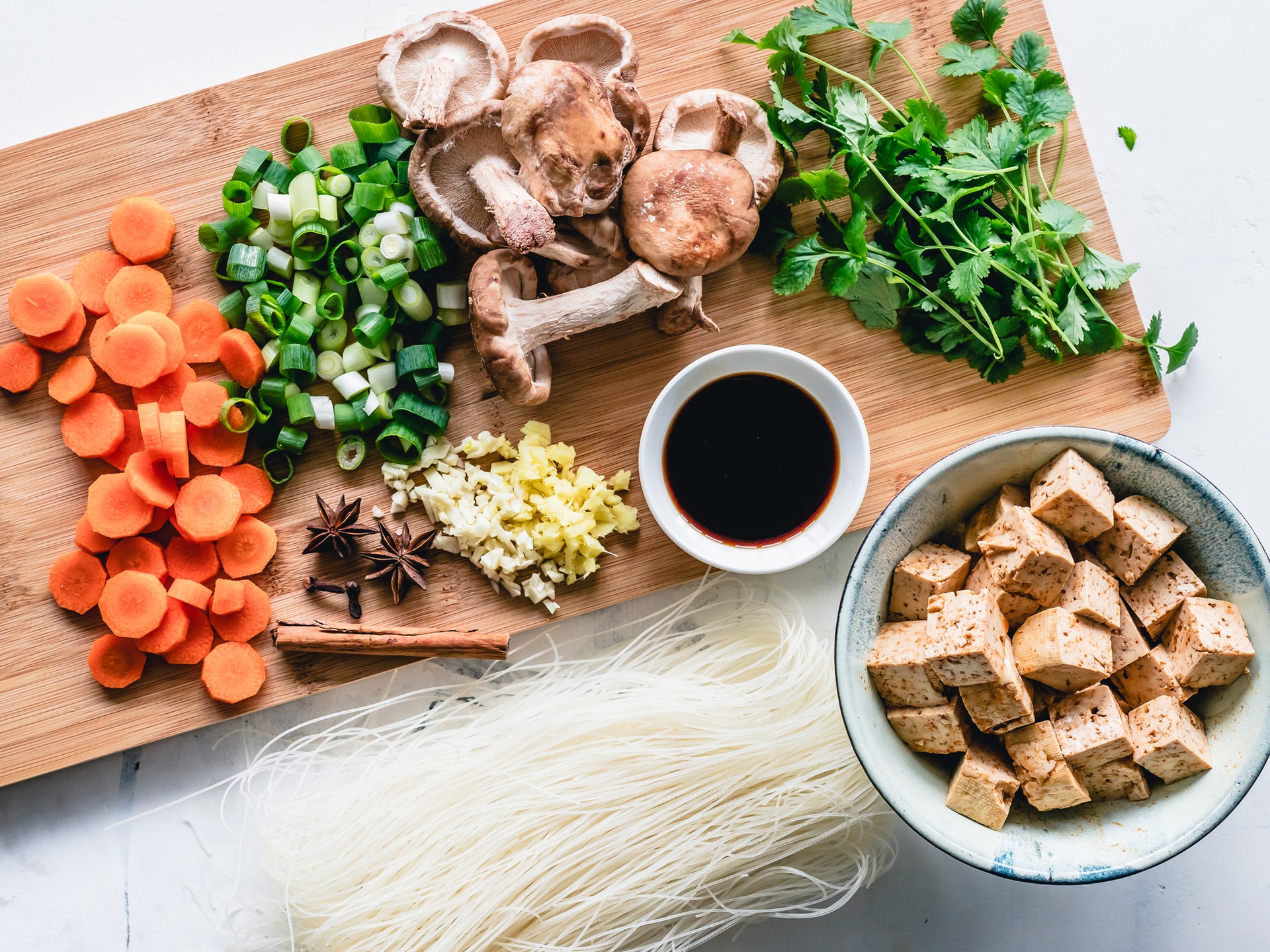 a cutting board of chopped ingredients including mushrooms carrots ginger garlic tofu and greens